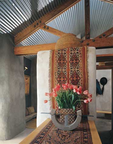 The utilitarian corrugated-steel roof rests atop recycled-wood trusses and stucco walls, whose interior consists of stacked-and-sewn straw bales, opposite below—all materials that starkly contrast with the richness of the Turkish kilim, here.